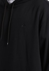 Zwarte hoodie van katoen, met een trekkoord, een voorzak en een subtiel reliëflogo op de linkerborst. Zachte textuur.