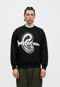 Μαύρη μπλούζα με μον�οχρωματικό γραφικό ενός αυτιού και μιας βίδας. Το σχέδιο έχει στρογγυλή εφαρμογή με ριμπ μανίκια και μέση.