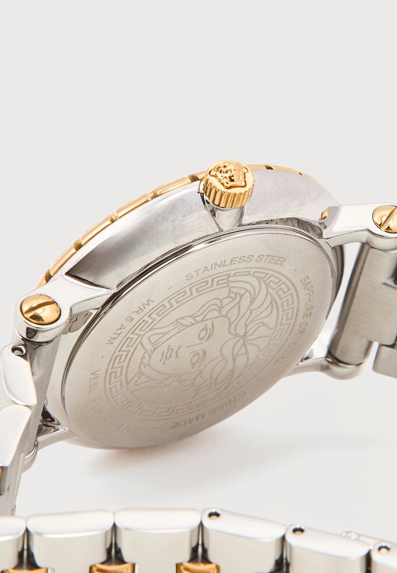 Dos du bracelet-montre en acier inoxydable bicolore affichant l'emblème de Méduse, la couronne en or, et le bracelet à maillons métalliques en argent et or.