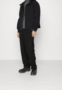 Black waterproof jacket with a hood, gray turtleneck, loose-fitting black trousers, and black boots with a textured sole.