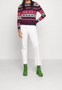 Röd och marinblå mönstrad tröja med snöflingor och renar, kombinerad med vita raka jeans och gröna mockaplatformstövlar.