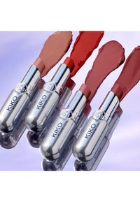 Four KIKO Milano lipsticks in silver tubes with smeared shades of nude, red, mauve, and rose on a reflective surface.