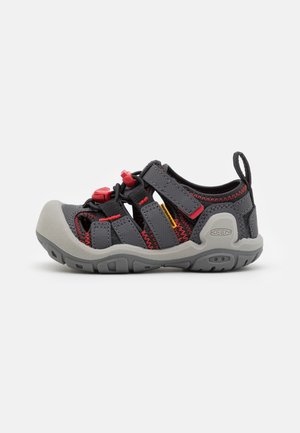 Zapatos de agua grises con correas negras y rojas, que cuentan con un diseño de puntera cerrada, cordones elásticos y una suela de goma para tracción.
