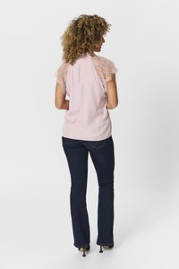 Blusa rosa con maniche in pizzo a cappuccio, abbinata a jeans a palazzo blu scuro. L'outfit presenta una texture di tessuto liscia e una silhouette aderente.