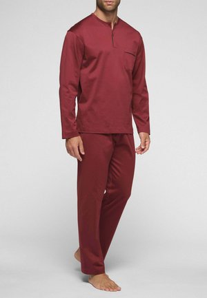 Uomo in piedi a piedi nudi che indossa un top a maniche lunghe e pantaloni abbinati di colore rosso scuro con tasca sul petto e colletto con bottoni.