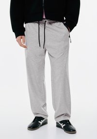 Grå sweatpants med snøre i taljen, tapered fit og sidelommer med lynlås. Bæres med sorte sneakers med hvide detaljer.