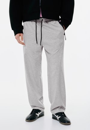 Gray sweatpants with a drawstring waist, tapered fit, and side zip pockets. Worn with black sneakers featuring white accents.