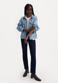 Giacca di jeans blu chiaro dal fit rilassato, con tasche anteriori e chiusura a bottoni. Abbinata a jeans blu scuro e stivaletti neri.