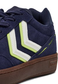 Granatowe zamszowe sneakersy z białymi i limonkowymi kanciastymi akcentami, brązową gumową podeszwą oraz teksturowanym kołnierzem z siateczki dla wygody.