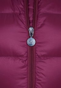 Burgundy puffer jacket featuring a front zipper with metallic EA logo pull and quilted texture, providing warmth and sleek design.