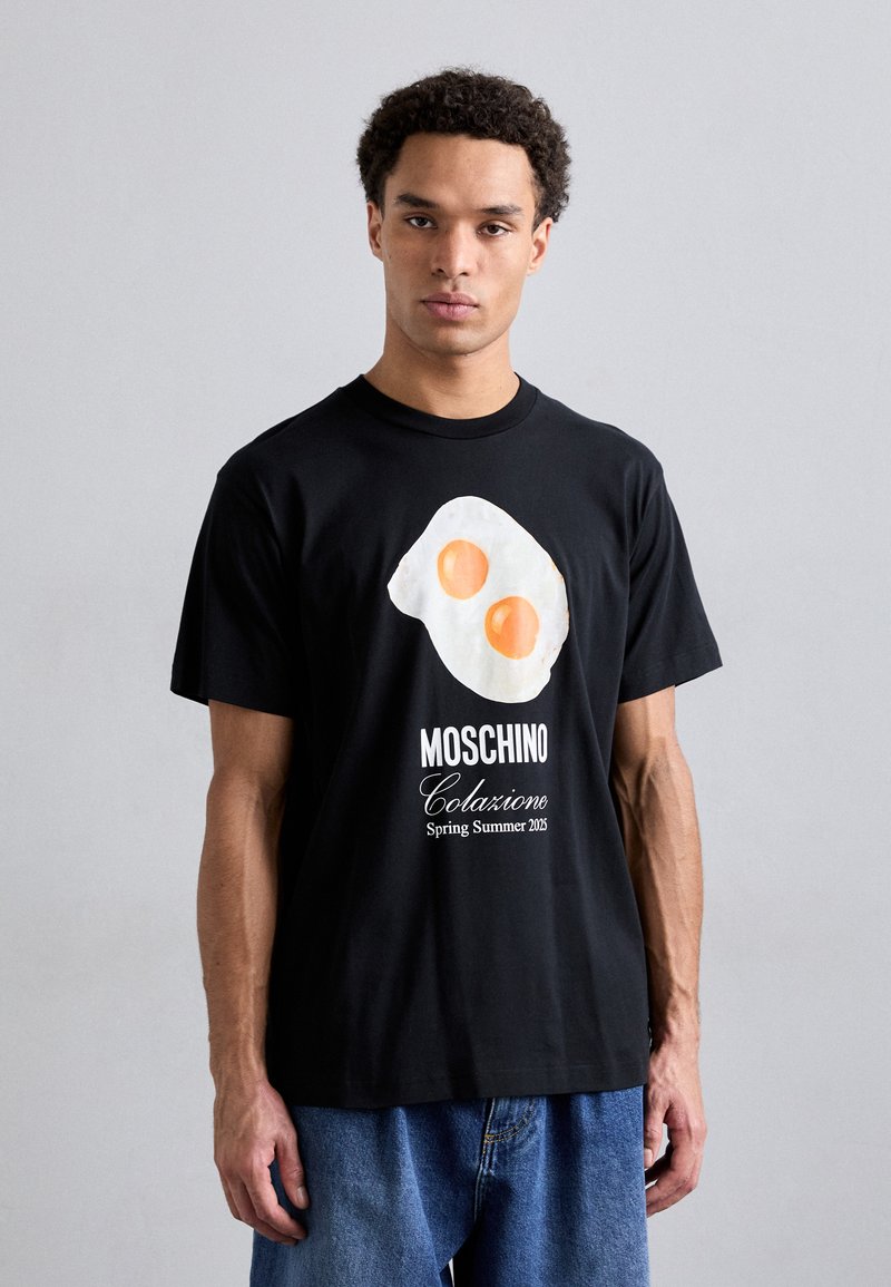 Black cotton T-shirt featuring a fried egg graphic in white and orange, with "Moschino Colazione Spring Summer 2023" text below.