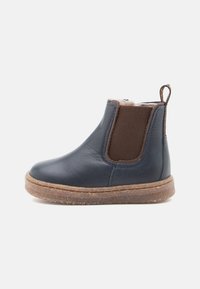 Botín Chelsea de cuero azul marino con paneles laterales elásticos marrones y suela de goma texturizada en marrón. Incluye una tira en la parte posterior para facilitar su calzado.