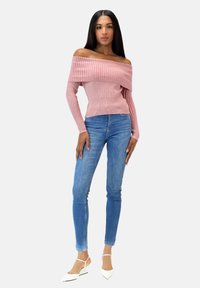 Rosa schulterfreier, gerippter Pullover mit langen Ärmeln, kombiniert mit blauen Skinny Jeans und weißen spitzen Flats. Glatte Stoffoberfläche.