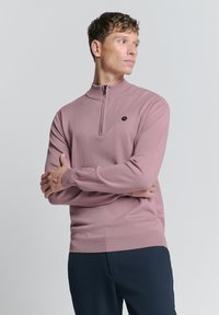 Lichtroze, pullover met ritssluiting gemaakt van gestructureerde stof. Heeft lange mouwen, geribbelde manchetten en een klein hexagonaal logo op de borst.