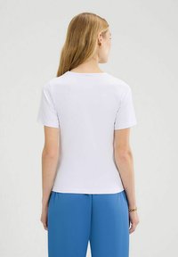T-shirt bianca a maniche corte con scollo tondo, texture in cotone e design aderente, abbinata a pantaloni blu.