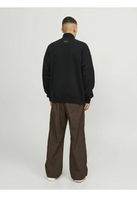 Sort sweatshirt med høj krave og afslappet pasform, sat sammen med brune brede bukser. Simpelt design uden synlige mønstre eller accenter.