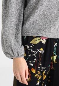 Grå stickad tröja med puffärmar, kombinerad med svarta byxor med blommönster i livfulla färger och olika blomsterdesigns.