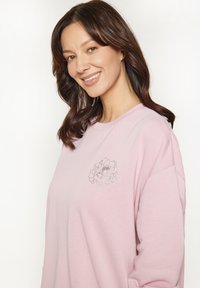 Sweatshirt rosa chiaro con un design floreale in ricamo argento nella zona sinistra del petto. Vestibilità morbida con scollatura rotonda e texture delicata.