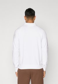Witte sweatshirt met een hoge kraag, geribbelde manchetten en onderzoom. Bevat zijstrepen en heeft een relaxte pasvorm, gecombineerd met bruine broek.