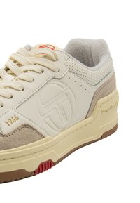 Leder-Sneaker in Creme mit beigen Wildlederakzenten, ausgestattet mit einem strukturierten Logo, durchbrochener Mesh und einer Gummisohle mit roten Details.
