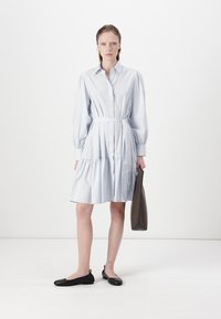 Abito camicia a righe blu chiaro con vita aderente, maniche lunghe e puffate, e gonna a balze. Abbinato a ballerine nere e una borsa grigia.