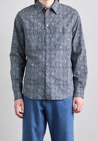 Langsleeve overhem met knopen in marineblauw met witte abstracte patronen, met een puntige kraag en bruine knopen. Gecombineerd met blauwe denim broek.