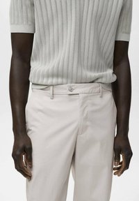 Un pull à manches courtes en maille côtelée gris clair associé à un pantalon droit beige pâle, doté d'une fermeture à boutons et d'une texture subtile.