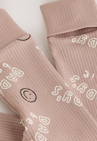 Ljus mauve-ribbade strumpor med vit abstrakt text och små svarta smiley-ansikten på enfärgad bakgrund.