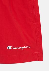 Crvene kratke hlače od lagane tkanine, sa bočnim šavovima i bijelim Champion logotipom otisnutim na donjoj lijevoj strani.