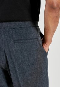 Mørkegrå skræddersyede bukser i tekstureret stof med en baglomme og en flad talje, kombineret med en sort top.