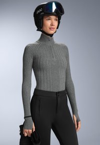 Grå, ribbad långärmad tröja med hög krage och liten framdragkedja; ihop med svarta tajta byxor och en svart skidhjälm med visir.