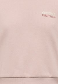 Sweatshirt rose en tissu doux, avec des poignets et un ourlet côtelés, portant l'inscription "ORIGINAL VARSITY club" brodée en blanc et bordeaux.