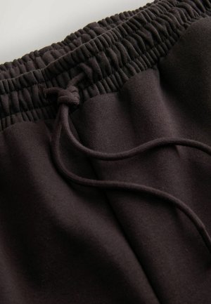Pantalon de survêtement noir avec une taille élastique et un cordon de serrage. Le tissu a une texture douce et lisse avec une coupe décontractée.