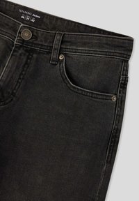 Jeans in denim nero con una texture liscia, caratterizzati da un classico design a cinque tasche e una chiusura con bottone in metallo. L'etichetta interna mostra i dettagli della taglia.