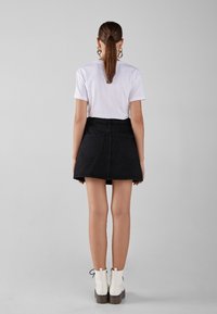 Black denim skirt with a flared design, two back pockets, worn with a white t-shirt and white ankle boots. Simple, clean lines with minimal detailing.