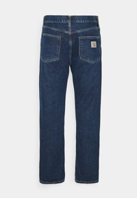 Jeans de mezclilla en azul oscuro con corte recto, que presentan un parche con el logo de Carhartt en el bolsillo trasero y detalles de costura visibles.