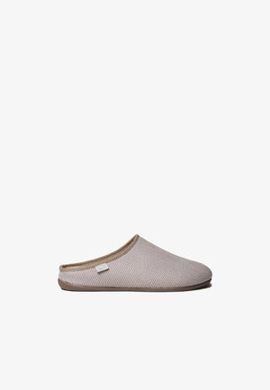 Beige, getextureerde instap-huisslof met lage achterkant en klein stoffen label aan de zijkant, in profiel te zien tegen een witte achtergrond.