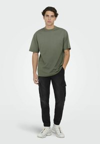 Olive green short-sleeve t-shirt paired with black cargo pants featuring side pockets, elastic cuffs, and white sporty sneakers.