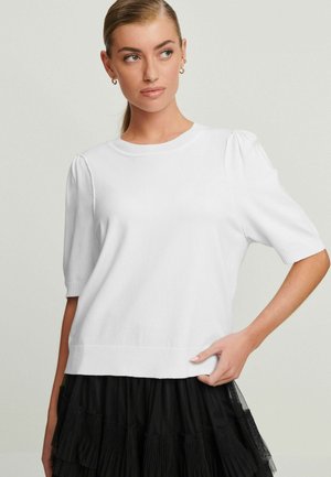 Hvid kortærmet sweater med ribbet halsudskæring og manchetter, der har pufærmer og en blød tekstur. Sættes sammen med en lagdelt sort nederdel.