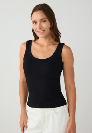 Zwarte geribde tanktop met brede banden en een ronde halslijn, met een aansluitend lijfje en een gladde textuur. Gepaard met witte shorts.