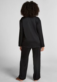 Zwarte satijnen pyjama set met een lange mouwen top met verticale streepjes en bijpassende losse broek, beide met een zachte textuur.