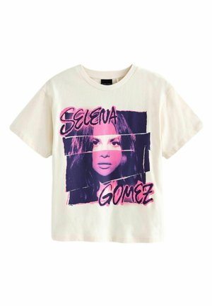 Cremfarbener T-Shirt mit einem grafischen Druck eines Frauen Gesichtes in Pink und Lila, mit den Namen "Selena" und "Gomez" in fettem Text.