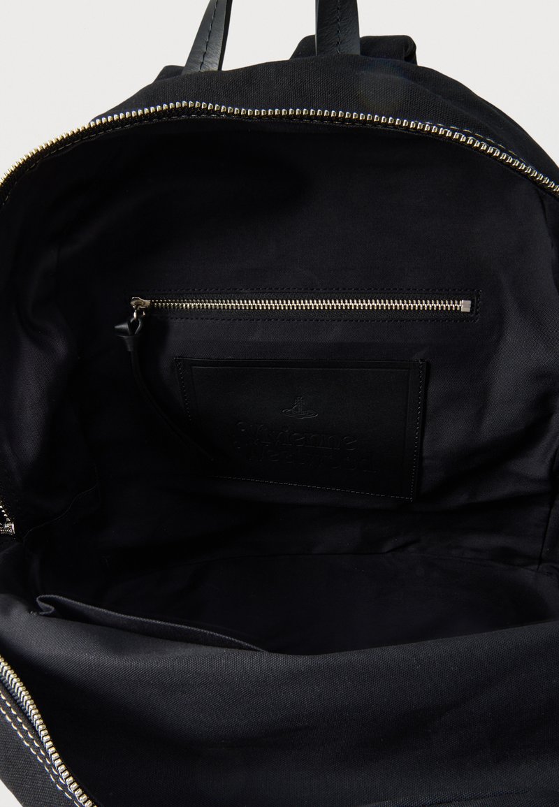 Sort rygsæks indre med en lynlåslomme, et åbent rum og læderhåndtag øverst.