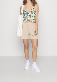 Top a maniche sottili verde con motivo floreale, pantaloni corti beige a coste e sneakers bianche. La texture è liscia e casual.