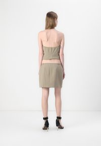 Kaki todelt sett med et strapless topp og et miniskjørt med hvite vertikale striper, sammen med svarte høyhælte sko.