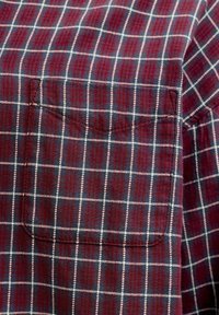 Tissu à carreaux rouges et bleus avec des lignes de quadrillage blanches présentant une poche poitrine rectangulaire cousue sur une chemise.