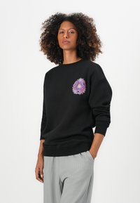Black sweatshirt with a colorful floral design on the chest, made from a soft fabric, featuring ribbed cuffs and hem. Paired with light grey pants.