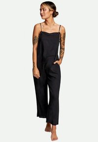 Jumpsuit noir en lin avec des bretelles spaghetti, coupe décontractée, jambes larges et poches latérales. Présente un design minimaliste et une texture douce.