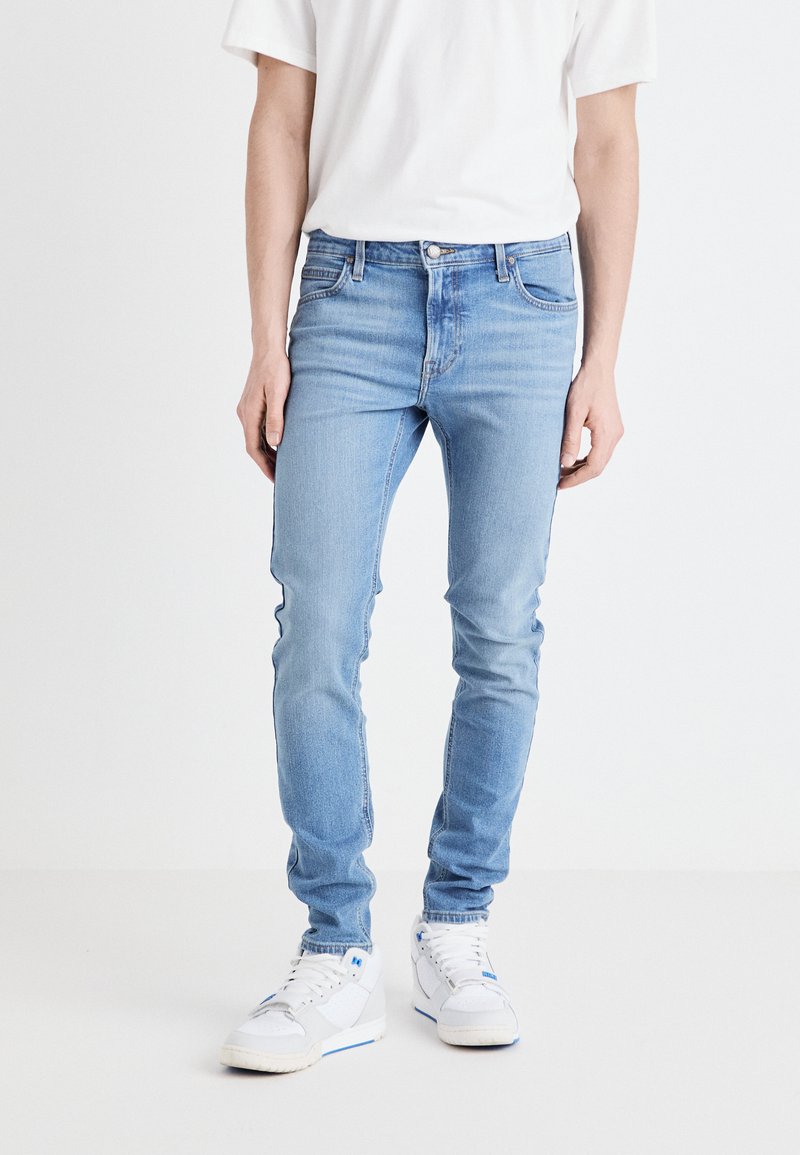 Jeans ajustados de color azul claro, hechos de denim, que cuentan con un diseño estándar de cinco bolsillos, presillas para cinturón y un ligero desgaste en los muslos.