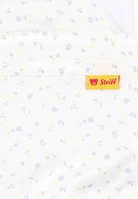 Tessuto in cotone con sfondo bianco caratterizzato da piccoli motivi floreali blu e gialli. Include un'etichetta rossa e gialla "Steiff".
